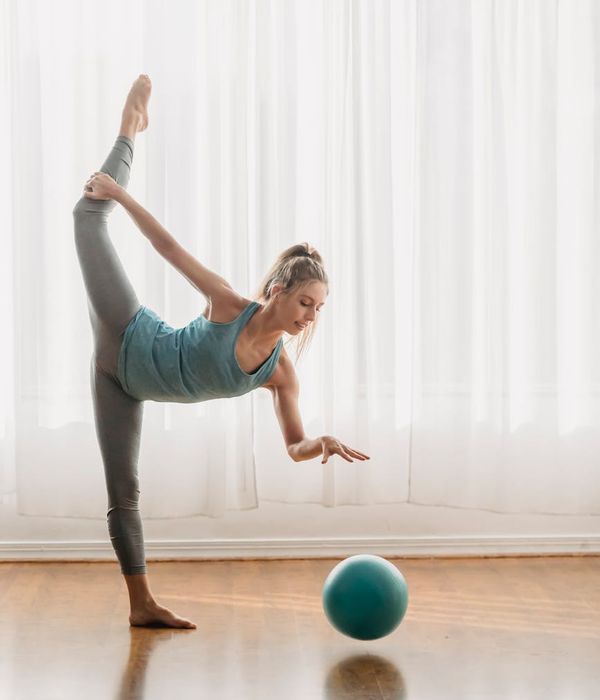 A woman in a balanced, graceful yoga pose, exuding calm and strength in a brightly lit studio.